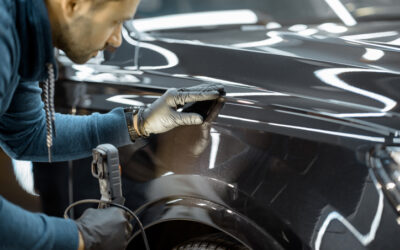 Car service worker examining vehicle body for scratches and damages, taking a car for professional auto detailing. Professional body car inspection concept